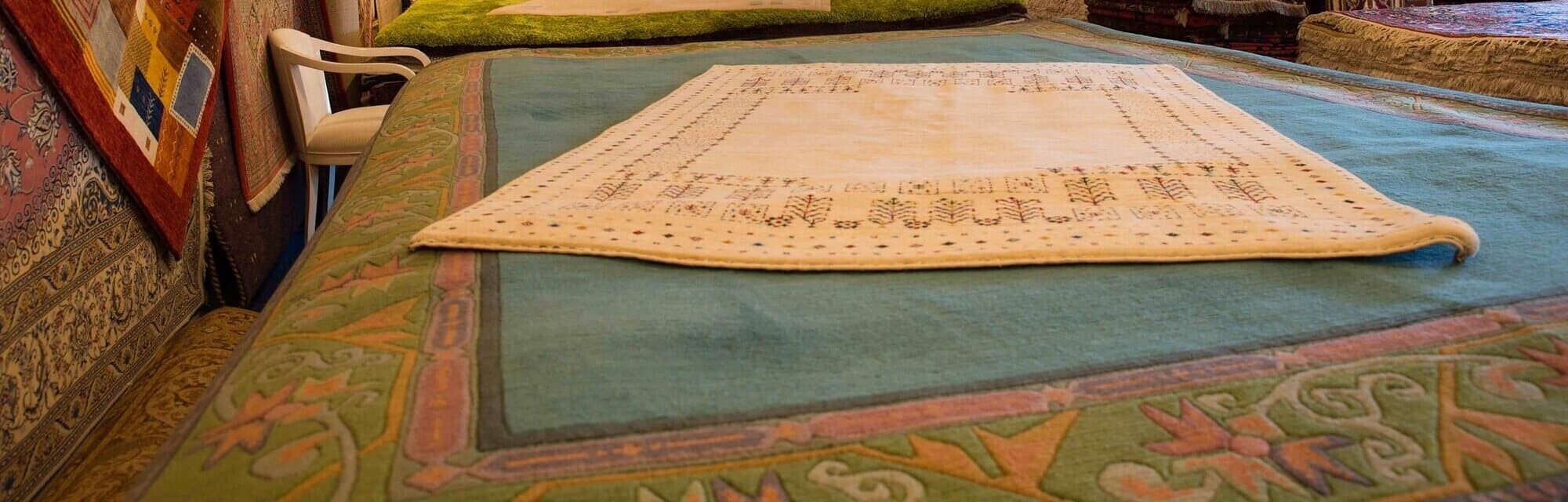 Heller Teppich, ausgelegt auf einem türkisfarbenen Teppich, links hängende Teppiche und ein weißer Stuhl