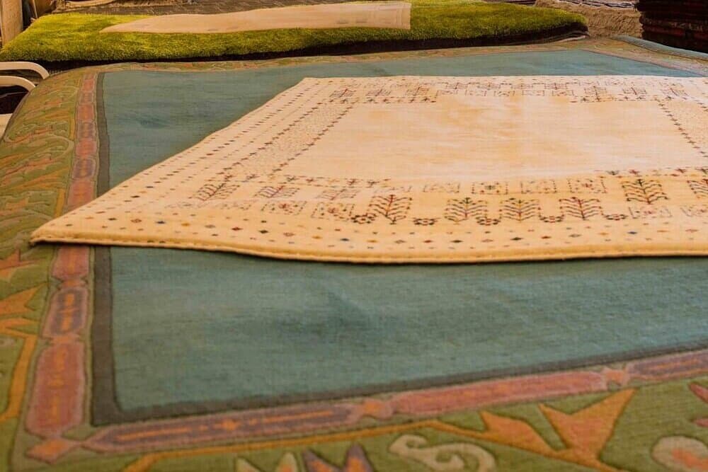 Heller Teppich mit feinen bunten Musterreihen, ausgelegt auf einem türkisfarbenen Teppich mit grüner Bordüre