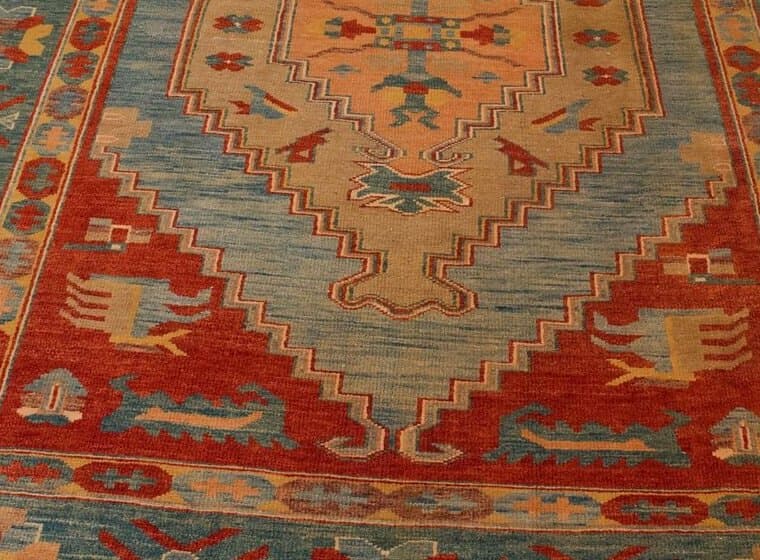 Nahaufnahme eines Teppichs mit gestuftem Medaillon in Sand und Hellblau auf rotem Grund, an den Seiten eine türkisfarbene Bordüre